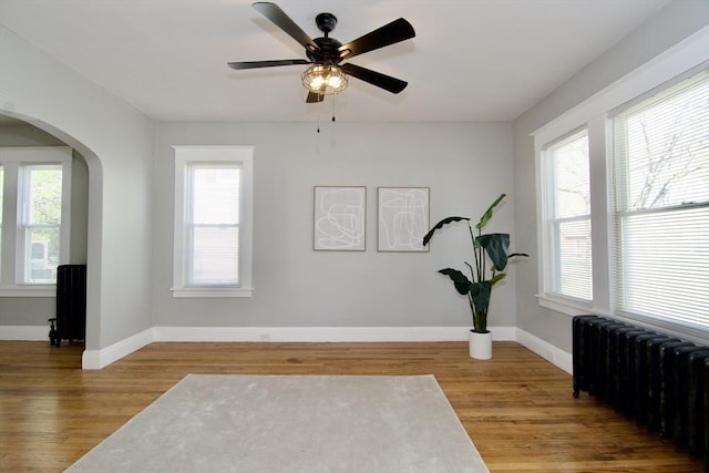 exercise area featuring wood finished floors, baseboards, arched walkways, and radiator