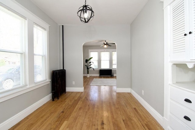 hallway featuring light wood finished floors, arched walkways, and baseboards