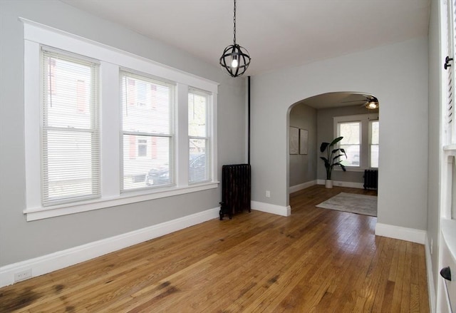 unfurnished dining area featuring radiator, a chandelier, baseboards, arched walkways, and wood finished floors