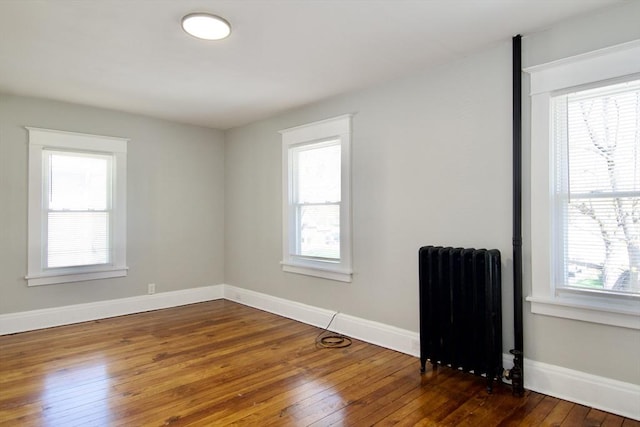 empty room with hardwood / wood-style floors, radiator heating unit, a wealth of natural light, and baseboards