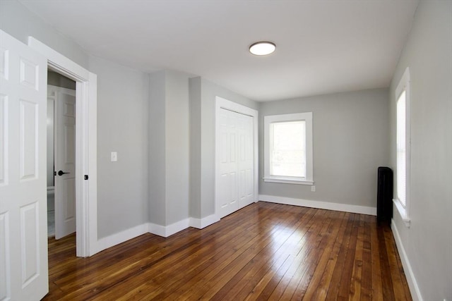 unfurnished bedroom featuring dark wood-type flooring, a closet, baseboards, and multiple windows
