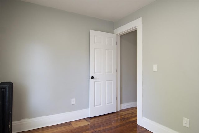 unfurnished room featuring dark wood-style floors, baseboards, and radiator