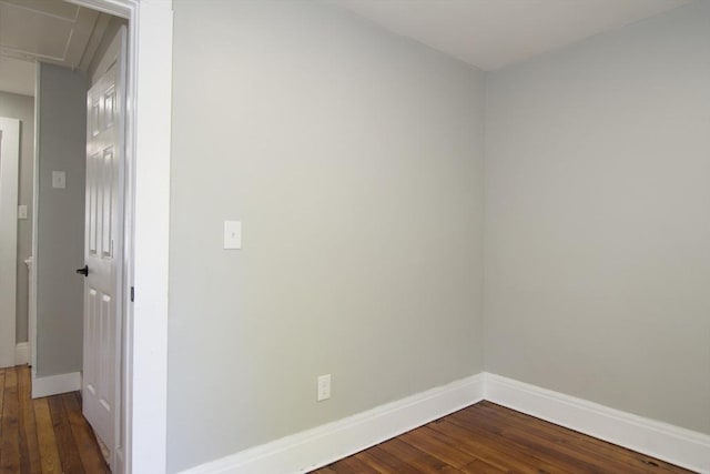 empty room with attic access, dark wood finished floors, and baseboards