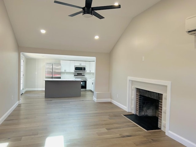 unfurnished living room featuring light wood-type flooring, a wall mounted AC, ceiling fan, high vaulted ceiling, and a fireplace