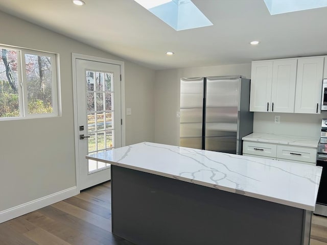 kitchen featuring a kitchen island, light hardwood / wood-style floors, vaulted ceiling with skylight, white cabinets, and appliances with stainless steel finishes