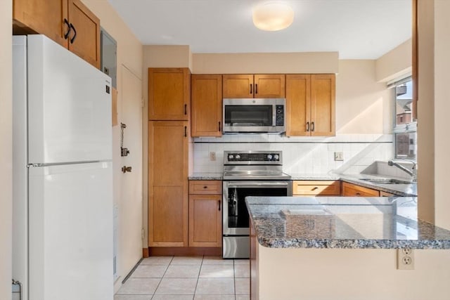 kitchen with light tile patterned floors, decorative backsplash, brown cabinets, stainless steel appliances, and a sink