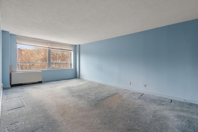 carpeted spare room with baseboards, a textured ceiling, and radiator heating unit