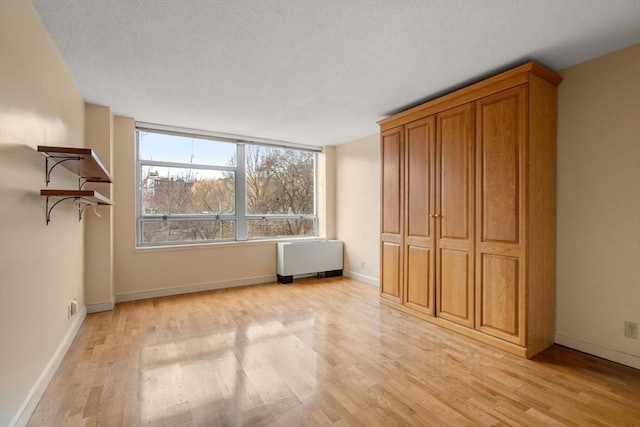 interior space featuring radiator heating unit, light wood-style floors, baseboards, and a textured ceiling