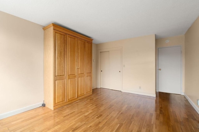 unfurnished bedroom with a closet, light wood-style flooring, a textured ceiling, and baseboards