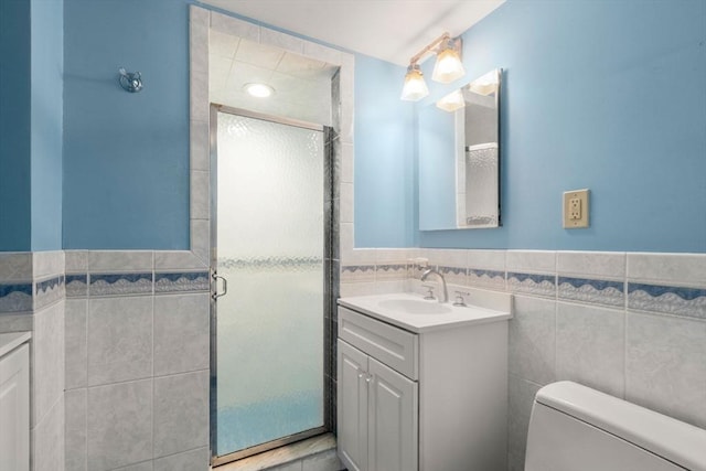 bathroom featuring toilet, vanity, wainscoting, a stall shower, and tile walls