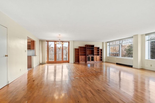 unfurnished living room with a notable chandelier, baseboards, and light wood-style floors