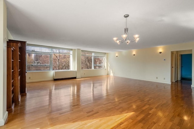 unfurnished living room with an inviting chandelier, radiator heating unit, wood finished floors, and baseboards