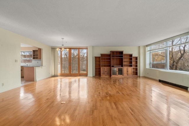 unfurnished living room featuring an inviting chandelier, light wood-type flooring, baseboards, and a sink