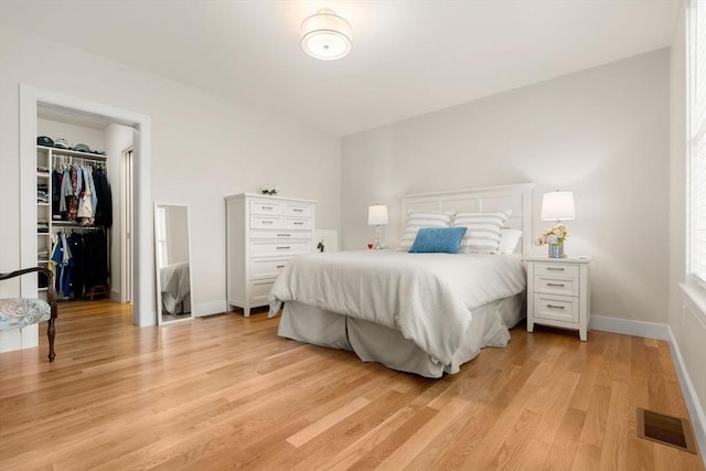 bedroom with visible vents, light wood-type flooring, baseboards, a closet, and a spacious closet
