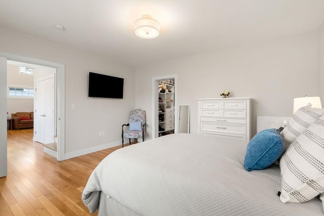 bedroom featuring a closet, baseboards, a walk in closet, and light wood-type flooring