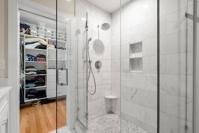 full bath featuring wood finished floors, a walk in closet, and a stall shower