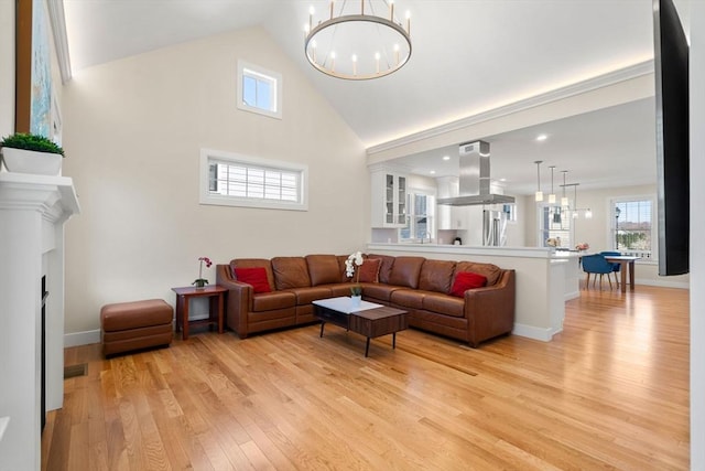 living area with baseboards, light wood-style flooring, a chandelier, and high vaulted ceiling