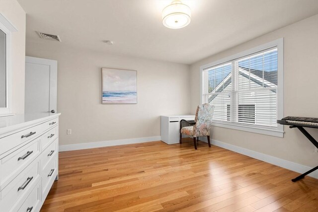 living area with baseboards, light wood-type flooring, and visible vents