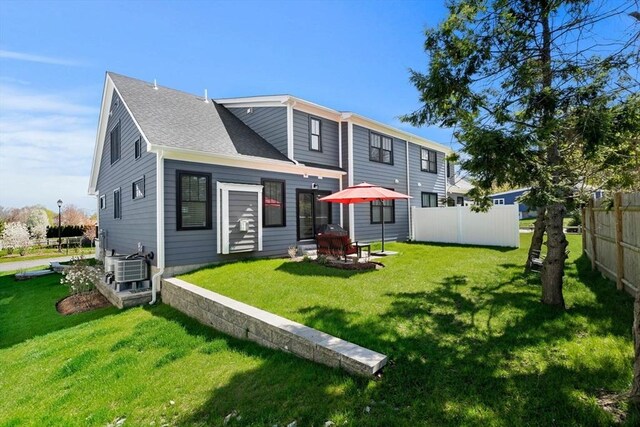 rear view of property featuring fence, central air condition unit, a yard, and roof with shingles