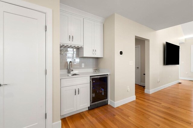 bar featuring a sink, light wood finished floors, baseboards, wine cooler, and backsplash