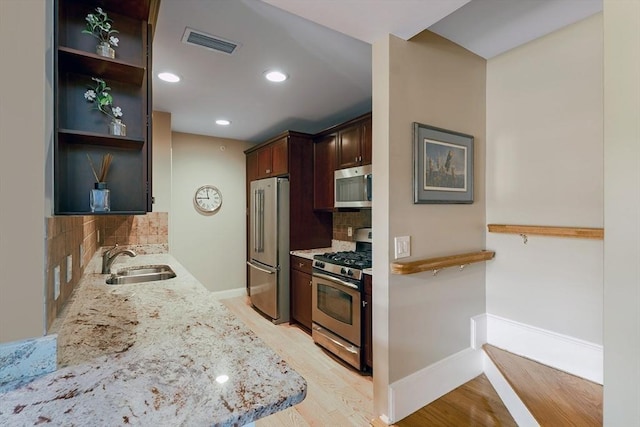 kitchen with light stone countertops, appliances with stainless steel finishes, decorative backsplash, sink, and light hardwood / wood-style flooring