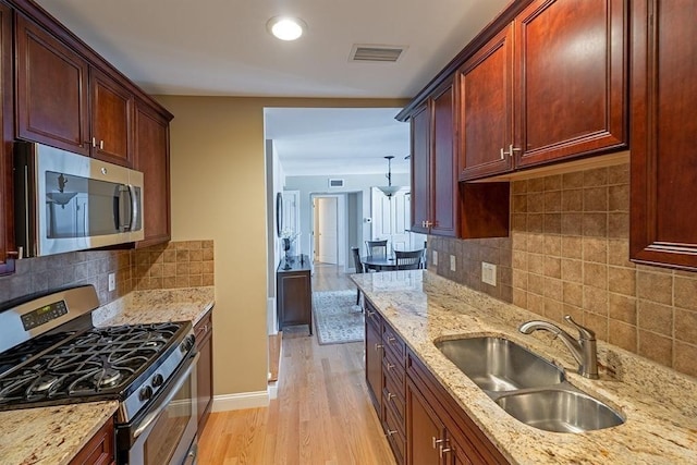 kitchen featuring light stone countertops, appliances with stainless steel finishes, sink, decorative light fixtures, and light hardwood / wood-style flooring