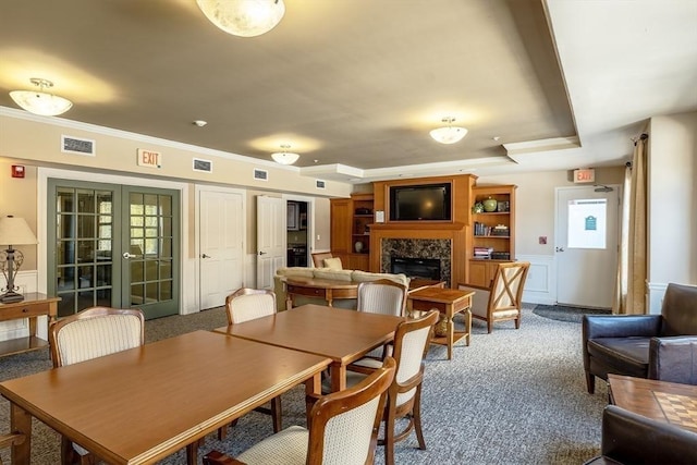 carpeted dining room featuring french doors, a tray ceiling, and a premium fireplace