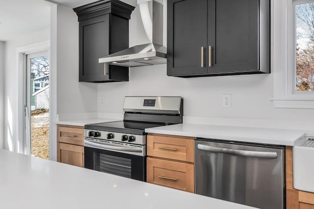 kitchen featuring stainless steel appliances, light countertops, wall chimney range hood, and dark cabinets