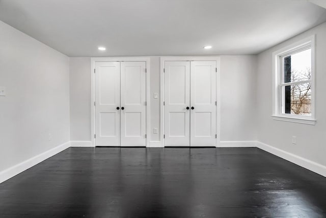 unfurnished bedroom featuring recessed lighting, baseboards, two closets, and dark wood-style flooring