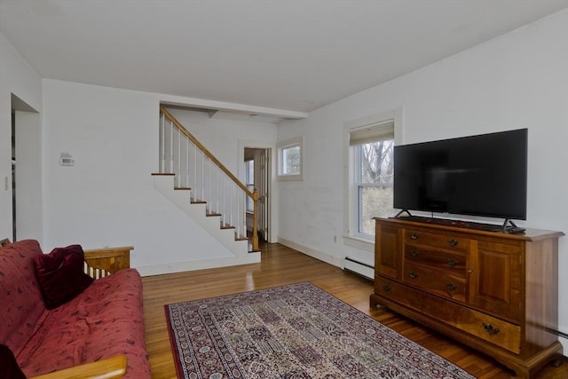 living area with a baseboard radiator, baseboards, wood finished floors, and stairs