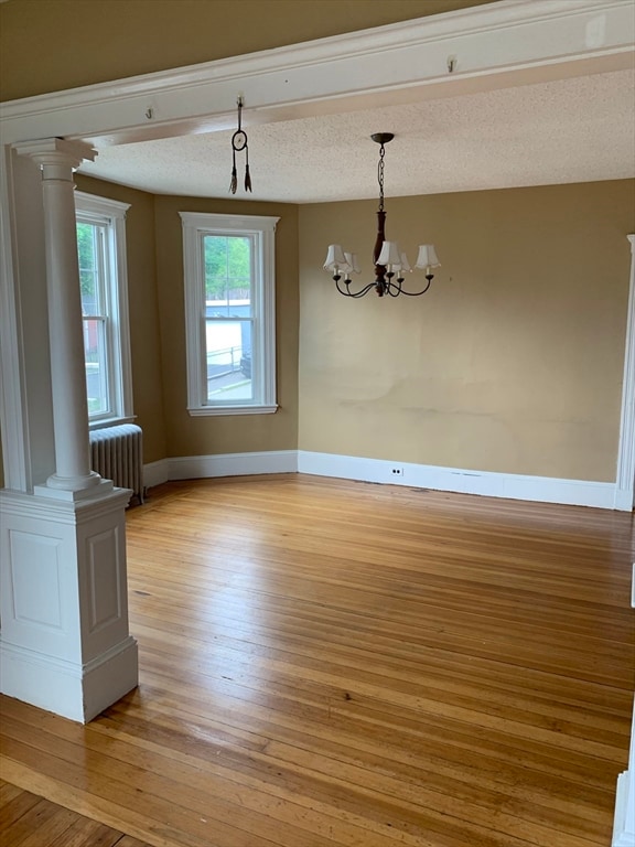 unfurnished dining area with radiator, light wood-type flooring, a textured ceiling, and an inviting chandelier