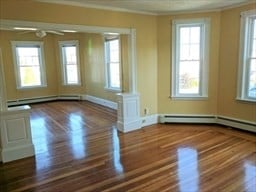 empty room featuring ceiling fan, a healthy amount of sunlight, crown molding, and dark wood-type flooring