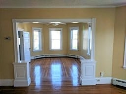 empty room with hardwood / wood-style floors, baseboard heating, crown molding, and ceiling fan