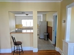 kitchen featuring stainless steel refrigerator, crown molding, hardwood / wood-style floors, a breakfast bar, and white cabinets