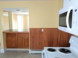 kitchen with white appliances, a baseboard radiator, and wood walls