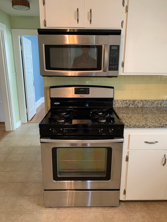 kitchen featuring light stone countertops, stainless steel appliances, light tile patterned floors, tasteful backsplash, and white cabinets