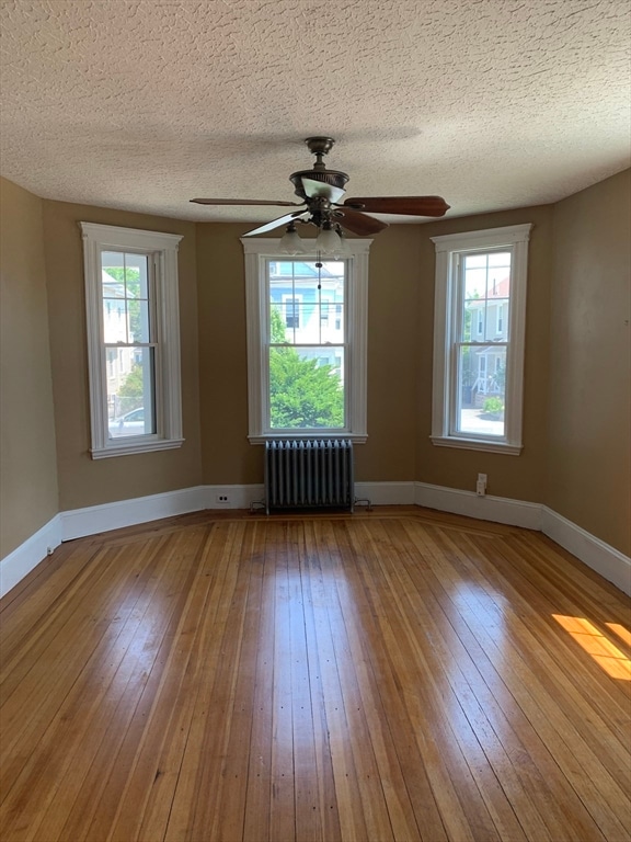 unfurnished room featuring radiator heating unit, a wealth of natural light, and wood-type flooring