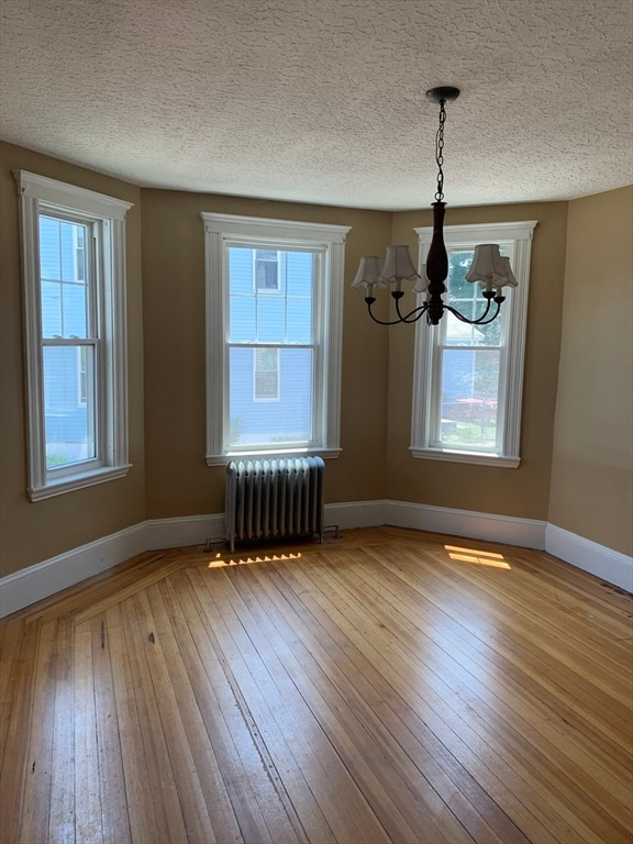 unfurnished dining area featuring a chandelier, a textured ceiling, hardwood / wood-style flooring, and radiator