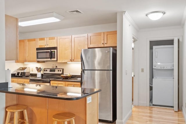 1818 Main St Unit 307, Holden, MA 01522 - kitchen featuring stainless steel appliances, estacked washer and dryer, a kitchen bar, light brown cabinets, and light wood-style flooring