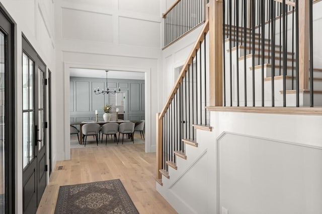 stairway with a towering ceiling, hardwood / wood-style floors, and a notable chandelier