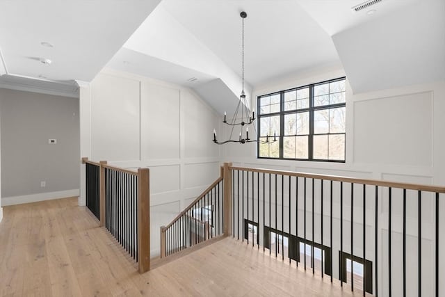 corridor featuring light wood-type flooring, crown molding, a chandelier, and vaulted ceiling