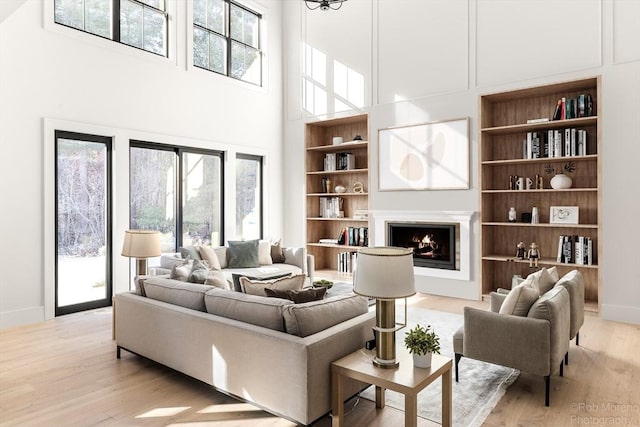 living room featuring a towering ceiling, light hardwood / wood-style flooring, and built in shelves