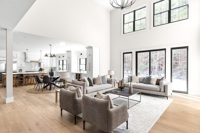 living room featuring light wood-type flooring, crown molding, a high ceiling, and a notable chandelier