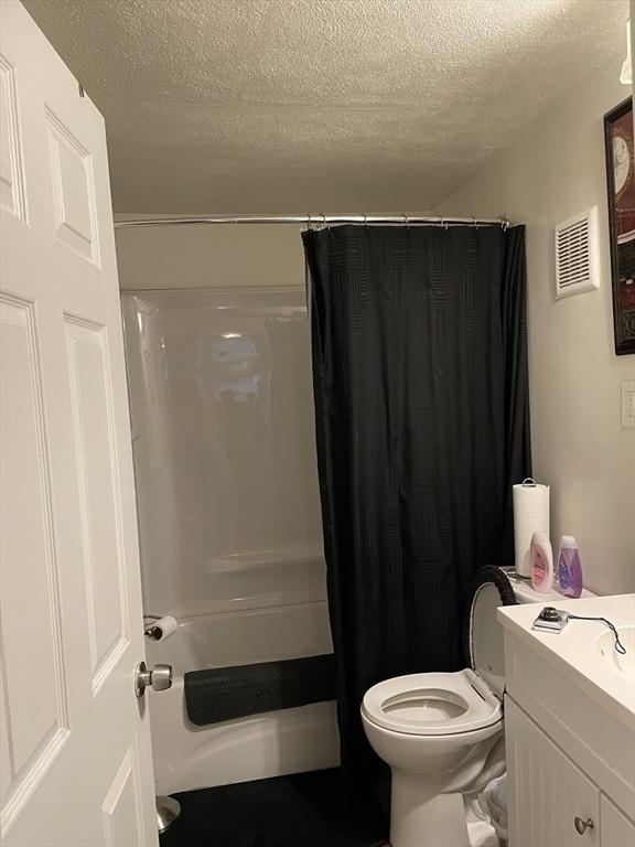 full bathroom with vanity, a textured ceiling, toilet, and shower / bathtub combination with curtain