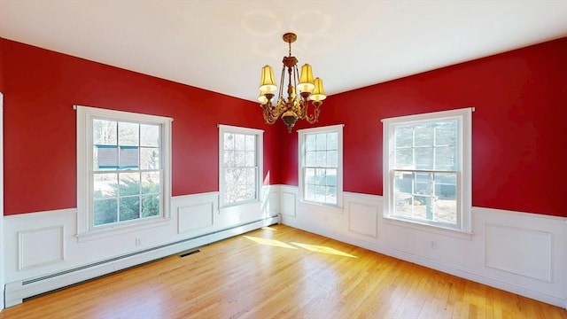 unfurnished dining area featuring a wainscoted wall, a notable chandelier, baseboard heating, and wood finished floors