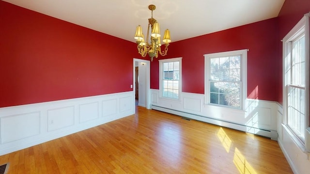 unfurnished room featuring light wood-type flooring, a wainscoted wall, a baseboard heating unit, and a chandelier