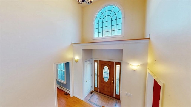 foyer with a baseboard radiator, a towering ceiling, and an inviting chandelier