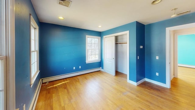 unfurnished bedroom with wood finished floors, visible vents, baseboards, a closet, and baseboard heating