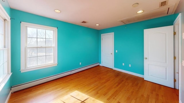 empty room featuring a baseboard heating unit, visible vents, wood finished floors, and attic access