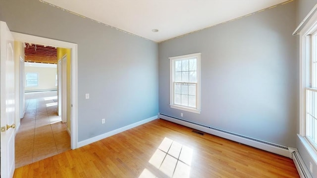 empty room featuring a baseboard heating unit, light wood-style floors, and baseboards